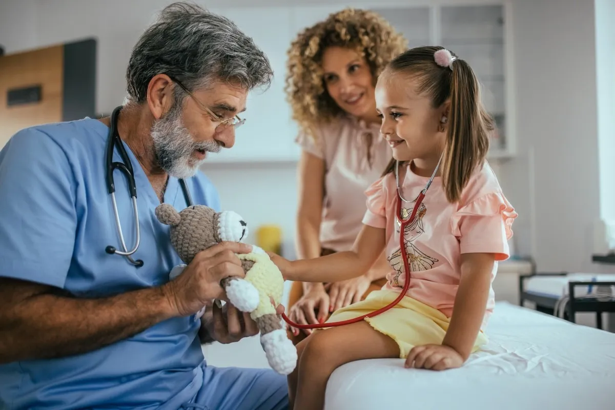 An FNP examining a young patient shows her a teddy bear.